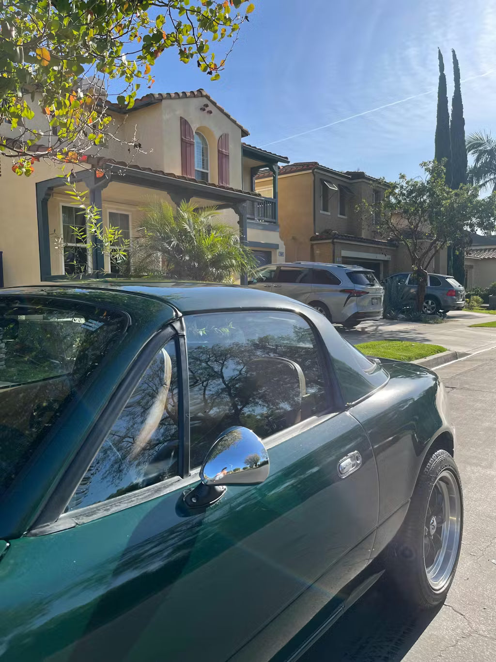 Green miata parked on a residential street with houses and trees in the background